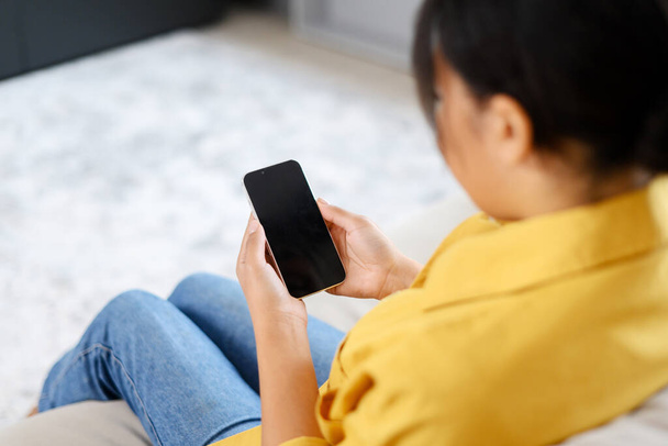 Back view a woman holding smartphone with an empty screen, woman sits on couch and holds gadget with blank display, mock-up, app advertising - Fotoğraf, Görsel