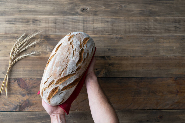 Hands showing a piece of rustic bread on wooden background with red napkin ornament. Copy space. Top view. - Foto, Bild
