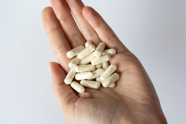Muchas cápsulas blancas en una mano de mujer. Suplementos dietéticos y medicamentos - Foto, imagen