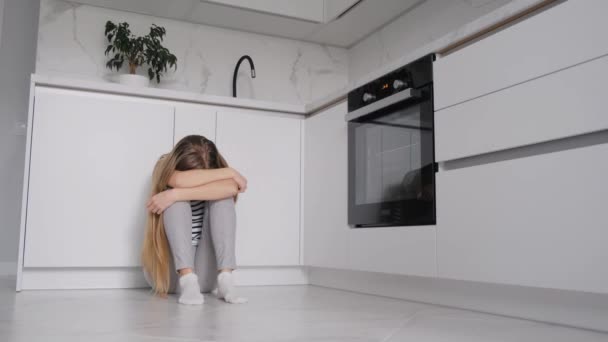 Kobieta cierpiąca na depresję, siedząca w kuchni, ukrywała głowę między kolanami. 4k wideo - Materiał filmowy, wideo