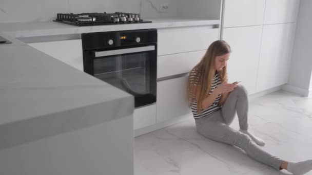 Žena trpící depresí, sedící v kuchyni, si schovala hlavu mezi kolena. Prochází si své sociální sítě, dívá se na fotky svých přátel a rodiny  - Záběry, video