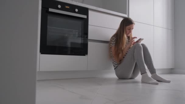 Eine Frau, die durch ihren Social-Media-Feed scrollt, leidet an Depressionen, sitzt in der Küche. 4k-Video - Filmmaterial, Video