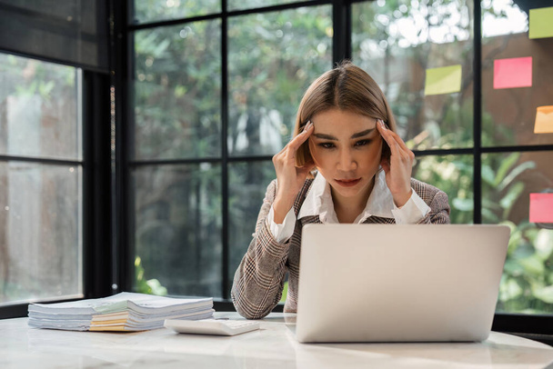 アジアの女性はノートパソコンで仕事をしながらストレスを感じています,オフィスで頭痛の種と疲れたアジアのビジネス女性,仕事で気分が悪く. - 写真・画像