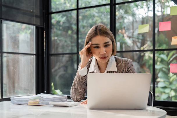 Las mujeres asiáticas están estresadas mientras trabajan en la computadora portátil, mujer de negocios asiática cansada con dolor de cabeza en la oficina, sentirse mal en el trabajo. - Foto, imagen