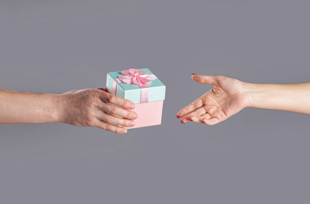 Mężczyzna i kobieta ręce trzymając różowe pudełko z prezentami. Dziewczyna daje prezent mężczyźnie. Kobiece dłonie trzymające prezent. Pudełko z prezentami w ręku, niespodzianka i pomysł na wakacje. Człowiek ręce gospodarstwa walentynki prezent. - Zdjęcie, obraz