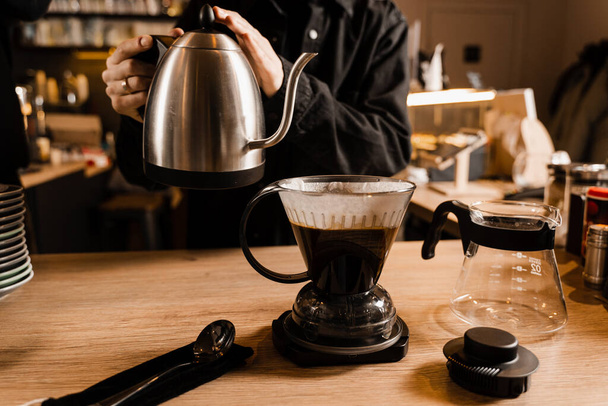 コーヒードリッパーをきれいにし、フィルターコーヒーの代替醸造方法を注ぐ。紙フィルターに含まれる焙煎・挽いたコーヒー豆にお湯をかける - 写真・画像