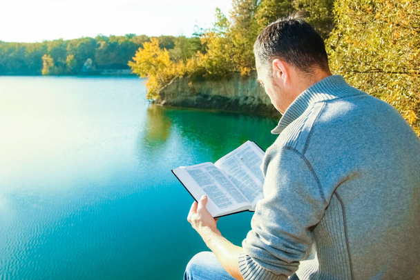 Happy guy reading a book in the park on nature travel education - Photo, image