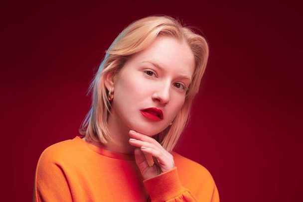 Studio shot of a serious blond woman posing on red background. - Valokuva, kuva