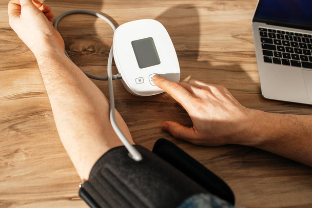 Zbliżenie męskich dłoni mierzących ciśnienie krwi specjalnym mankietem i tonometrem. Ocena stanu zdrowia w domu. Niedociśnienie tętnicze i nadciśnienie tętnicze - Zdjęcie, obraz