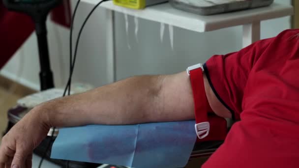 Közelkép egy érszorítóval megkötözött férfi kezéről. A beteg felkészítése véradásra egy donorközpontban. - Felvétel, videó