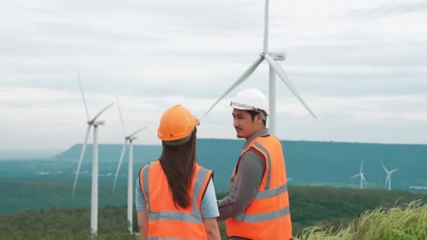 Mannelijke en vrouwelijke ingenieurs werken op een windmolenpark op de top van een heuvel of berg op het platteland. Progressief ideaal voor de toekomstige productie van hernieuwbare, duurzame energie. - Video