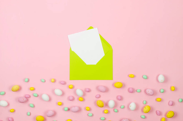 Colorful candy easter eggs on pastel pink background and light green envelope with blank card with place for text. Easter holiday and tradition concept.  - Foto, Imagem