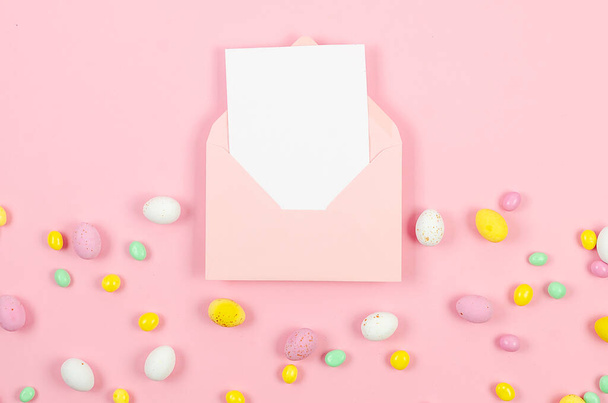 Colorful candy easter eggs on pastel pink background and pink envelope with blank card with place for text. Easter holiday and tradition concept.  - Foto, Imagem