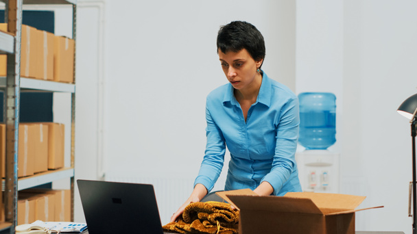 Young entrepreneur arranging products in cardboard boxes, shipping merchandise order to customers. Employee working on supply chain management and distribution, quality control. Handheld shot. - Fotografie, Obrázek