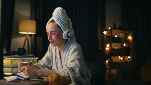 Positive lady singing dancing at home workplace closeup. Smiling bathrobe woman making notes listening music in evening. Freelancer girl with under eye patches relaxing having fun at night room - Photo, Image