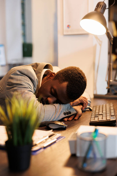 Müder Manager mit Burnout-Syndrom, der wegen extremer Müdigkeit am Schreibtisch schläft. Erschöpfter Geschäftsmann leidet nach nächtlicher Arbeit an Firmenprojekt unter Schläfrigkeit - Foto, Bild