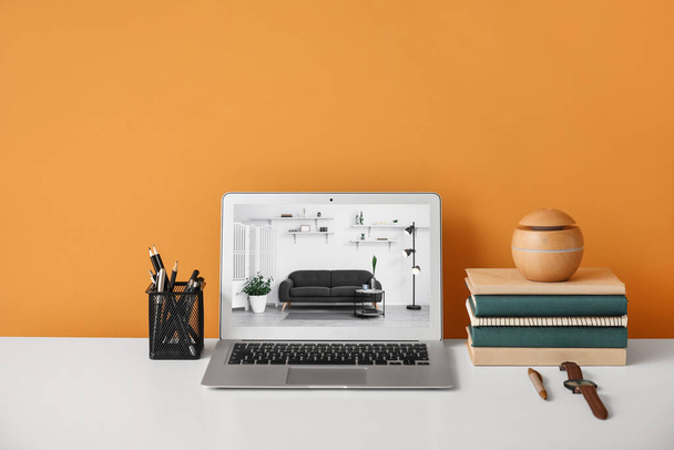 Laptop met open pagina van online meubelwinkel op tafel bij oranje muur - Foto, afbeelding