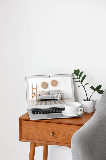 Стол и ноутбук с открытой страницей интернет-магазина мебели возле белой стены - Фото, изображение