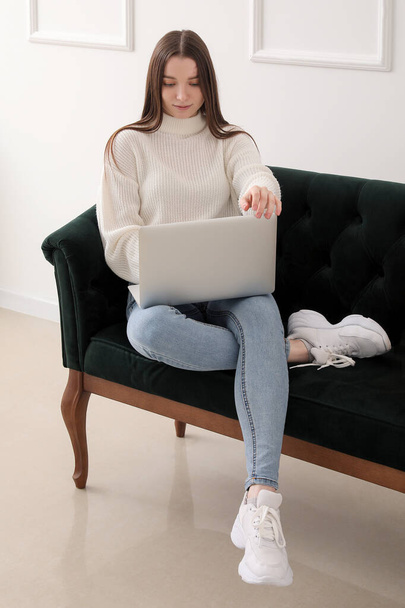 Young woman using laptop on green sofa near light wall - Foto, afbeelding
