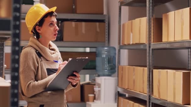Vrouwelijke werknemer controleren lijst van producten in depot, werken aan voorraad logistiek met papieren en het tellen van pakketten op rekken. Opslagruimte manager onderzoekt kartonnen dozen voor verzending. - Video