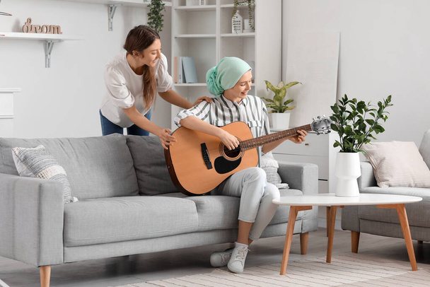 Teenage girl after chemotherapy playing guitar with her sister at home - Foto, Bild