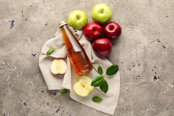 Lasipullo tuoretta omenaviinietikkaa ja harmaalla pohjalla olevia hedelmiä - Valokuva, kuva
