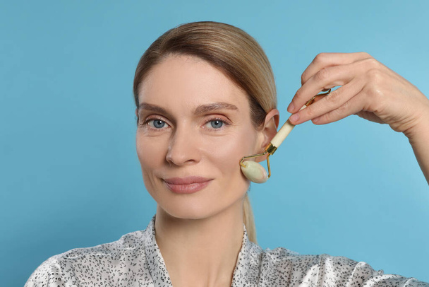 Woman massaging her face with jade roller on turquoise background - Φωτογραφία, εικόνα