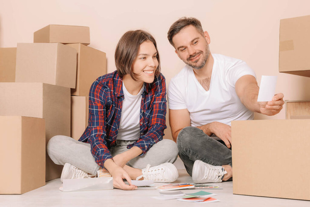 Happy couple surrounded by moving boxes choosing colors in new apartment - Foto, afbeelding