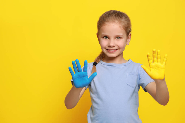 Little girl with hands painted in Ukrainian flag colors on yellow background, space for text. Love Ukraine concept - 写真・画像