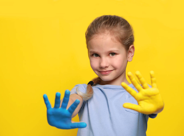 Little girl with hands painted in Ukrainian flag colors on yellow background, space for text. Love Ukraine concept - Фото, зображення