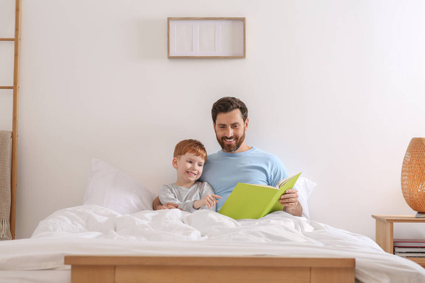 Father reading book with his child on bed at home - Φωτογραφία, εικόνα