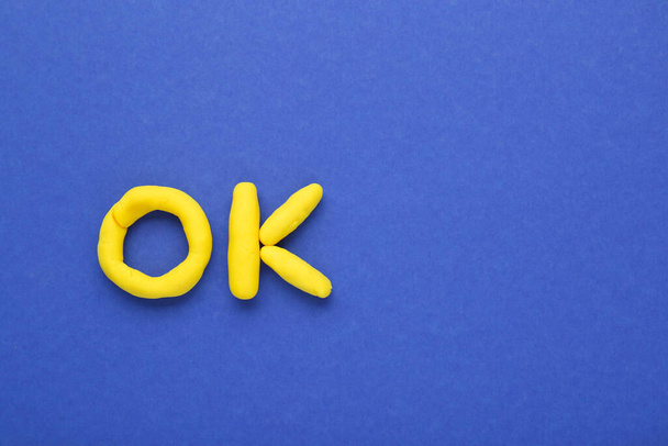 Word Ok aus gelbem Knetmasse auf blauem Hintergrund, Draufsicht. Raum für Text - Foto, Bild