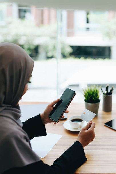 Beautiful Muslim woman shopping online using her phone and credit card. - Zdjęcie, obraz