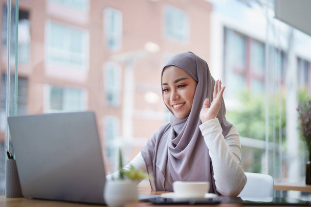 Kaunis musliminainen käyttää tietokonetta tervehtimään osallistujia videoneuvottelun kautta. - Valokuva, kuva