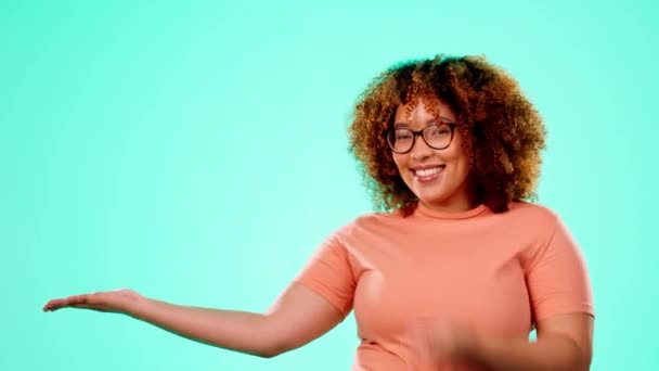 Face, pointing and black woman in studio with mockup space for promotion, advertising or announcement. Happy, smile and African female model showing mock up for product placement by blue background - Footage, Video