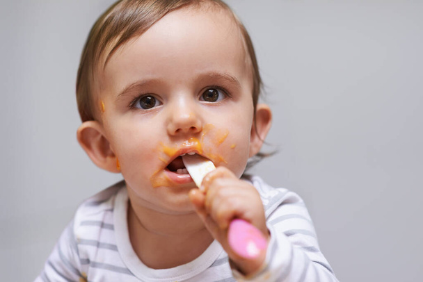 Messy and adorable. a cute little baby girl eating with a spoon - Fotoğraf, Görsel