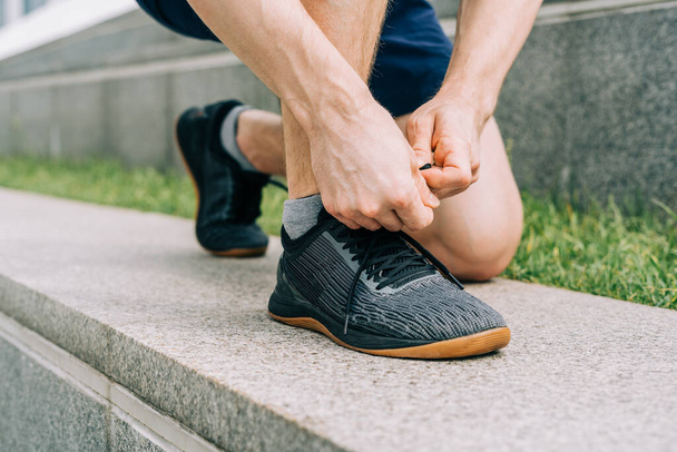 Закрыть спортивный человек завязывая шнурки во время бега на открытом воздухе. - Фото, изображение