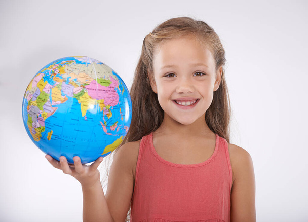 Eines Tages werde ich um die Welt reisen. Studioaufnahme eines entzückenden kleinen Mädchens, das einen Globus hält und in die Kamera lächelt - Foto, Bild