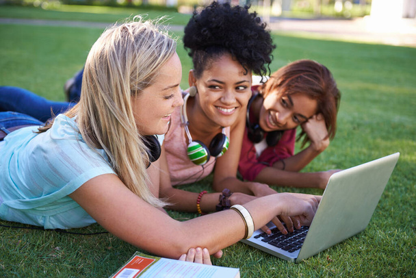 Учеба была смешной. Трое молодых студентов лежат на траве в парке и пользуются ноутбуком - Фото, изображение