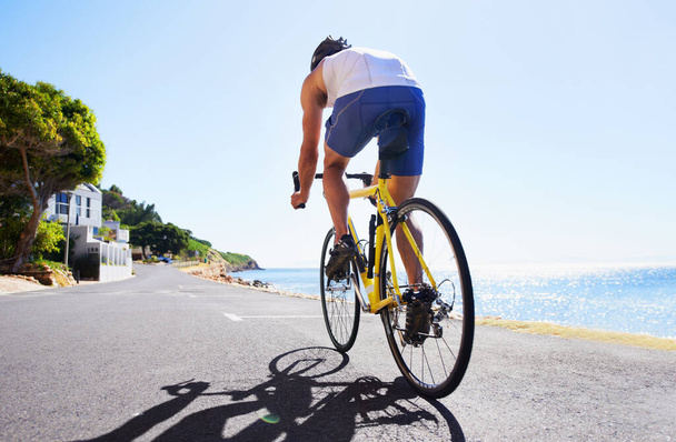 Enjoying the scenery while exercising. Cropped view of a cyclist cycling along an ocean road - Фото, изображение