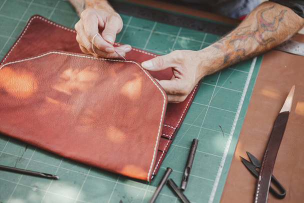 Nahaufnahme Handarbeit Prozess Leder Handarbeit in der Lederwerkstatt. Der Mensch hält Werkzeug in der Hand und arbeitet. Er näht Hammer, um eine Brieftasche zu machen. Gerber in der alten Gerberei. - Foto, Bild