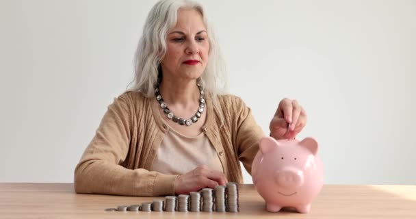 Starší žena s šedivými vlasy dávat mince do prasátka banky 4k film zpomalit. Koncept důchodového spoření - Záběry, video