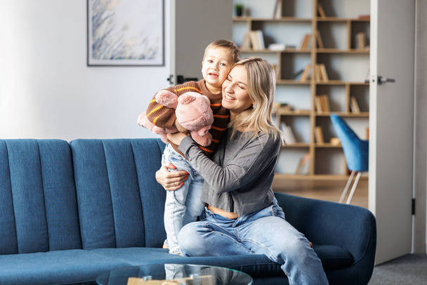 Young pregnant woman and her son sit on sofa at home, little boy spend time together, enjoy communication feeling kicks of unborn baby - Foto, imagen