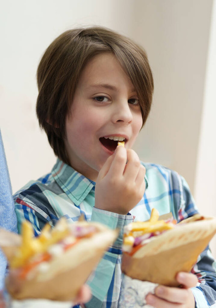 Happy white boy eats fast food for lunch. Portrait of cute elementary age kid enjoying gyros snack in a Greek restaurant - Photo, Image