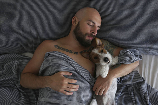 Portrait of a bearded man sleeping in bed with his wire haired jack russell terrier. Emotional support animal concept. Adult male and his dog napping together. Close up, copy space, background. - Foto, imagen