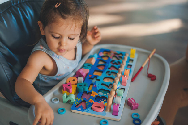 Cute baby girl sitting in a childs chair playing with educational wooden toys. Adorable caucasian infant. - Foto, Imagem