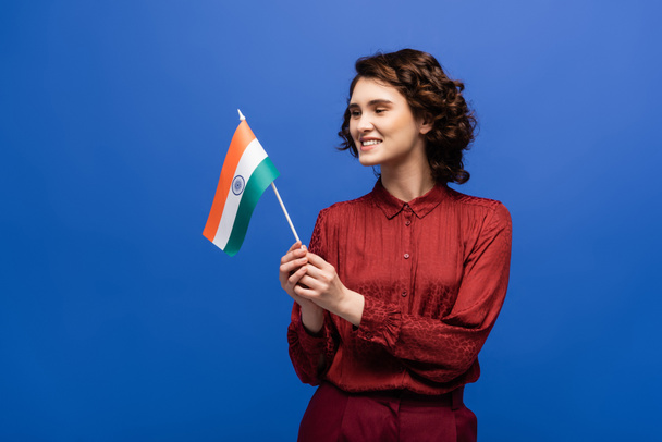 cheerful language teacher holding flag of India and looking at camera isolated on blue  - Foto, afbeelding