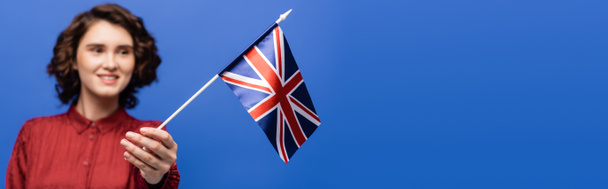 glücklicher Student mit lockigem Haar mit Blick auf die Flagge Großbritanniens auf blauem Banner  - Foto, Bild
