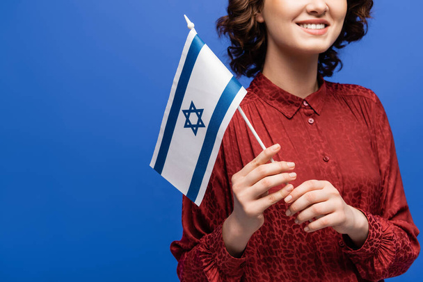 обрезанный вид улыбающейся учительницы иврита с флагом Израиля, изолированным на голубом - Фото, изображение