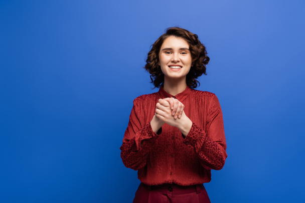 cheerful woman showing gesture meaning friendship on sign language isolated on blue - Foto, immagini